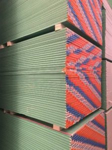 Large stack of green drywall panels with branded red and blue edges, showing compact vertical arrangement.