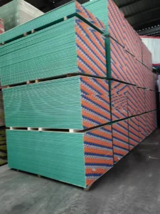 Large stack of green drywall panels organized in a warehouse, showcasing orderly arrangement and vibrant colors.