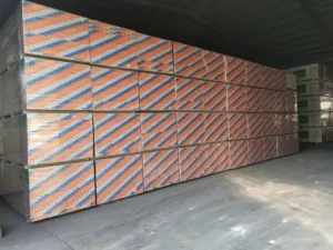 Large stack of drywall panels with orange and blue striped packaging in a warehouse setting.