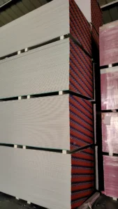 Large stacks of drywall sheets neatly arranged in a warehouse, with visible spacing for stability.