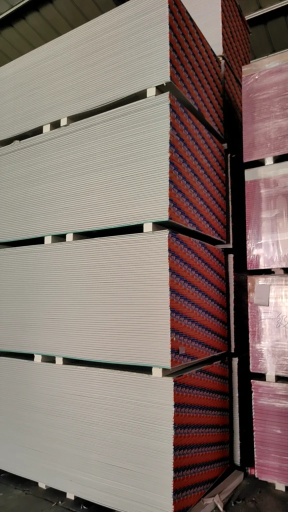 Large stacks of drywall sheets neatly arranged in a warehouse, with visible spacing for stability.